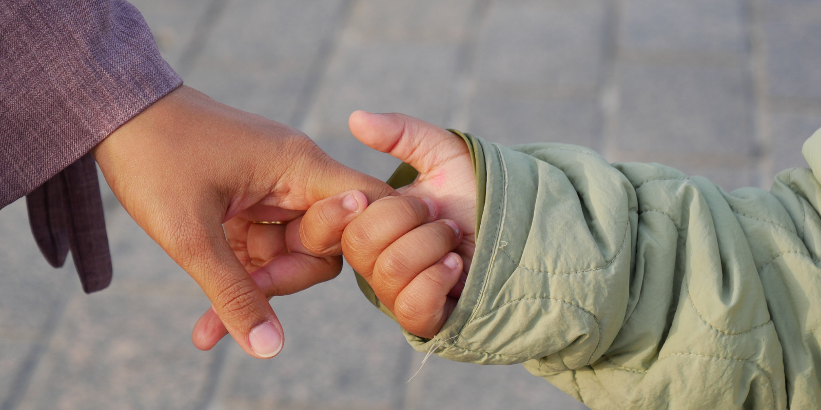Close-up of a mom and child holding hands on the sidewalk.
